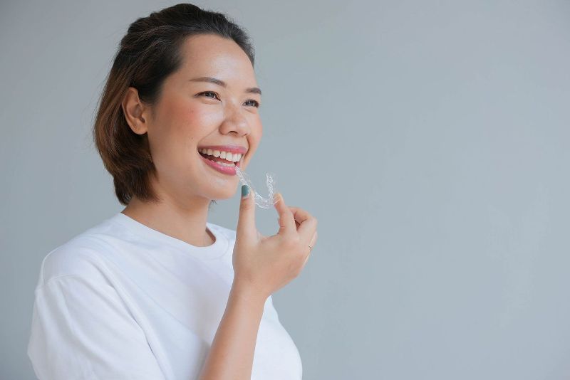 A woman is smiling while holding a clear brace on her teeth.