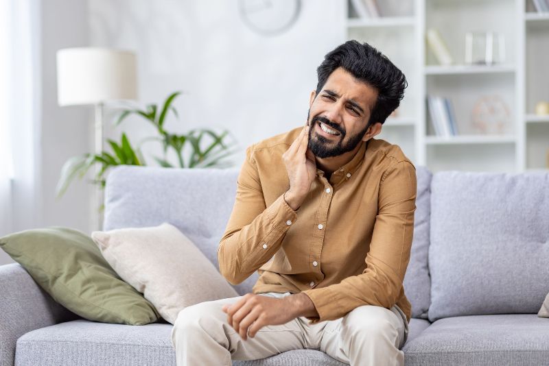 A man is sitting on a couch with a toothache.