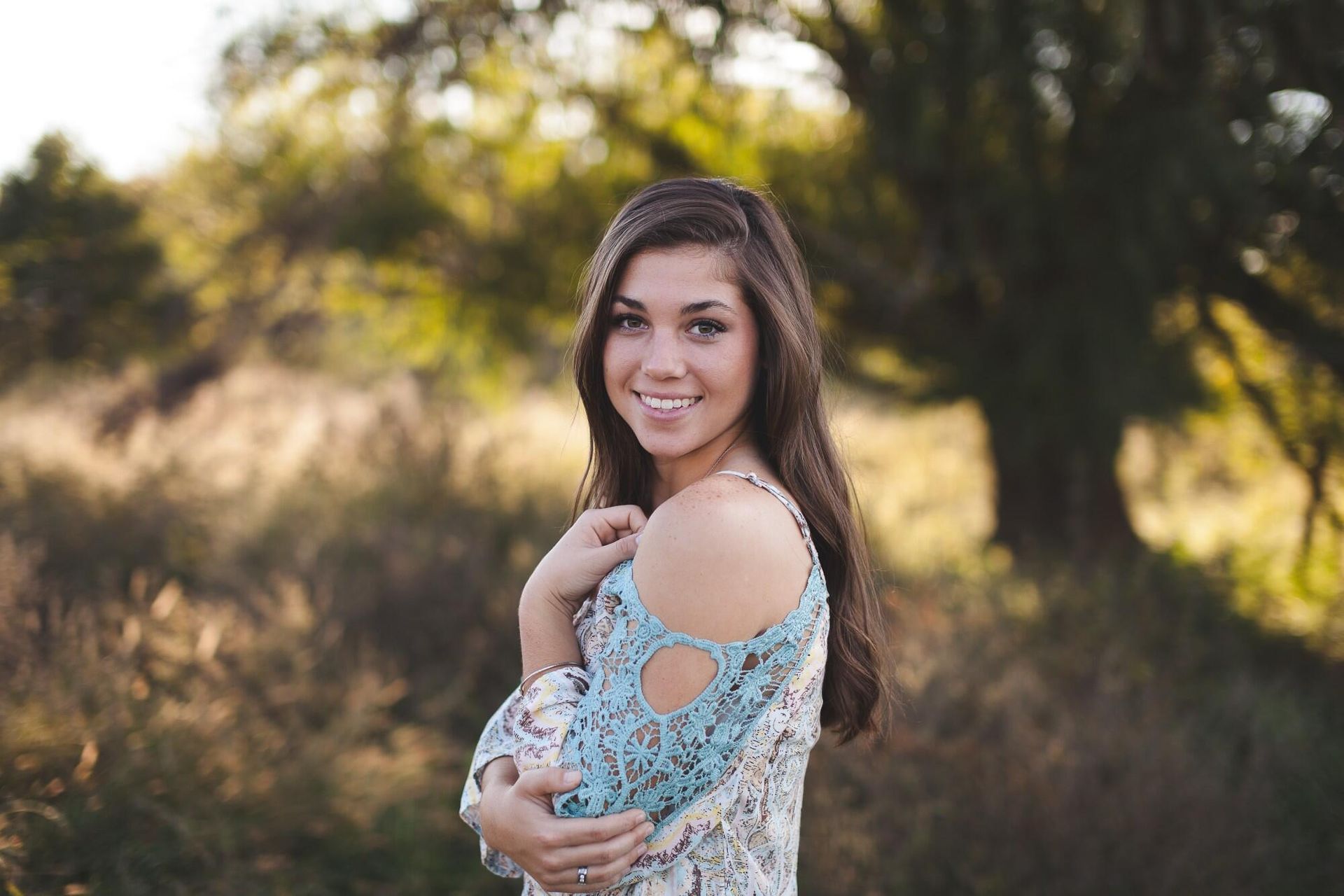 A woman in a blue off the shoulder top is standing in a field.