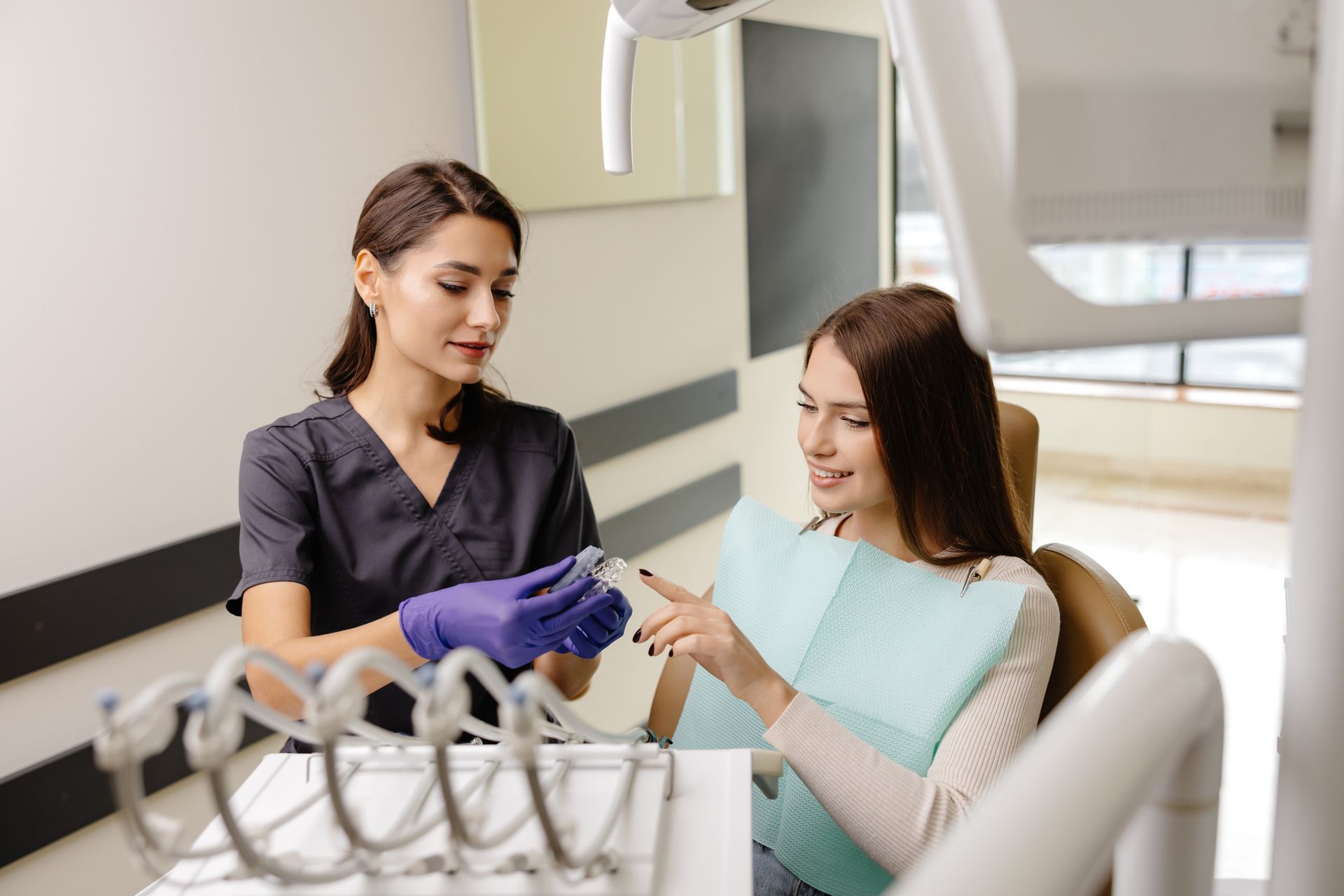 Dentist explaining a dental tool to a patient in a dental chair. They are in a brightly lit office.