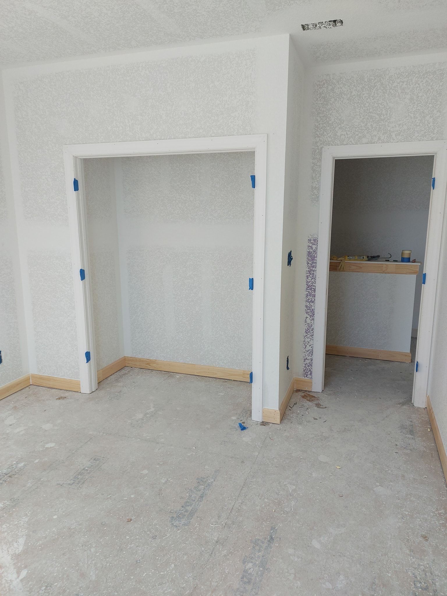 Unfinished room with taped-off doorway and a smaller opening to a work area, bare floor and walls.
