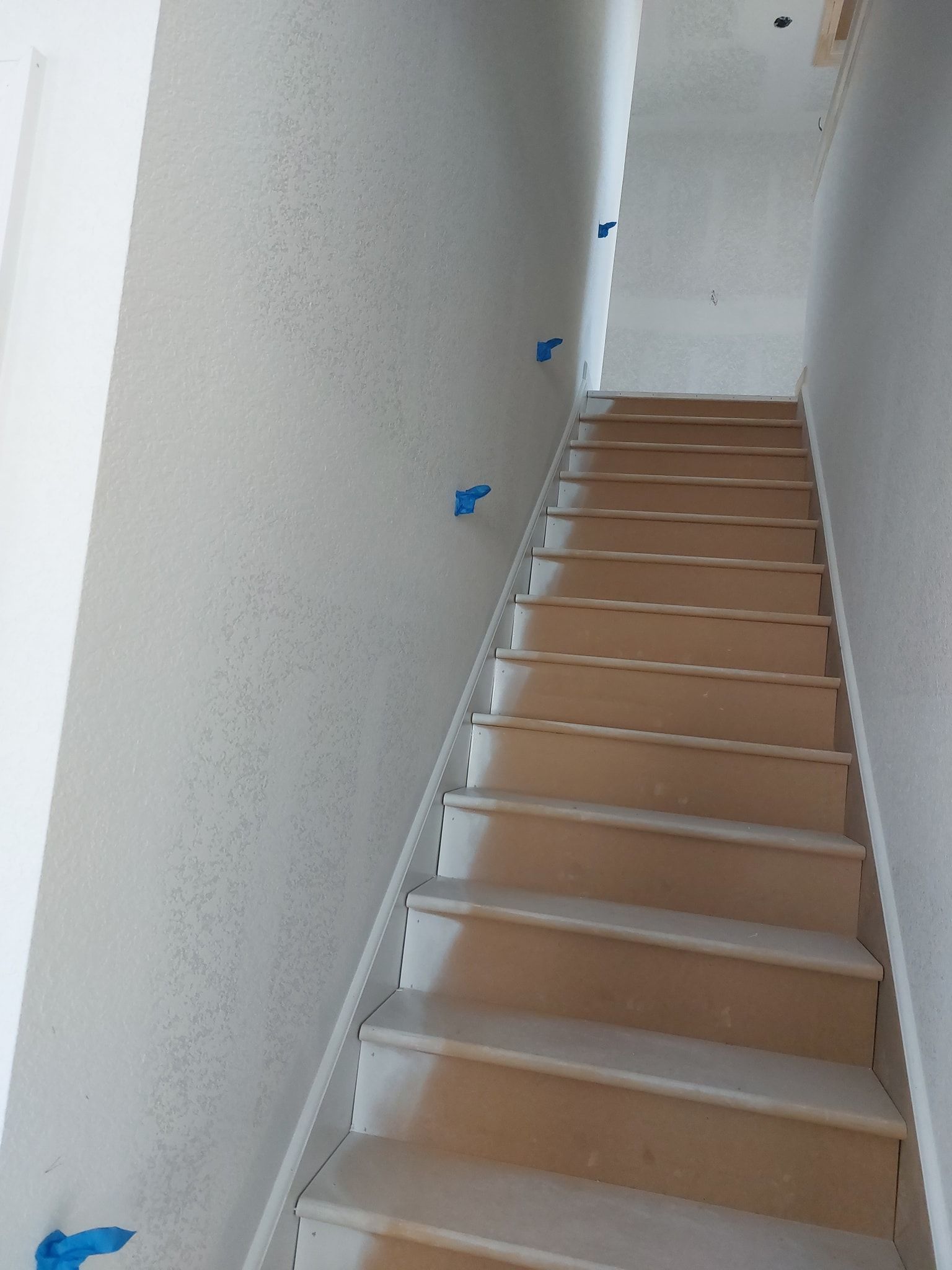 Narrow indoor staircase with white walls, brown steps, and blue wall-mounted markers.