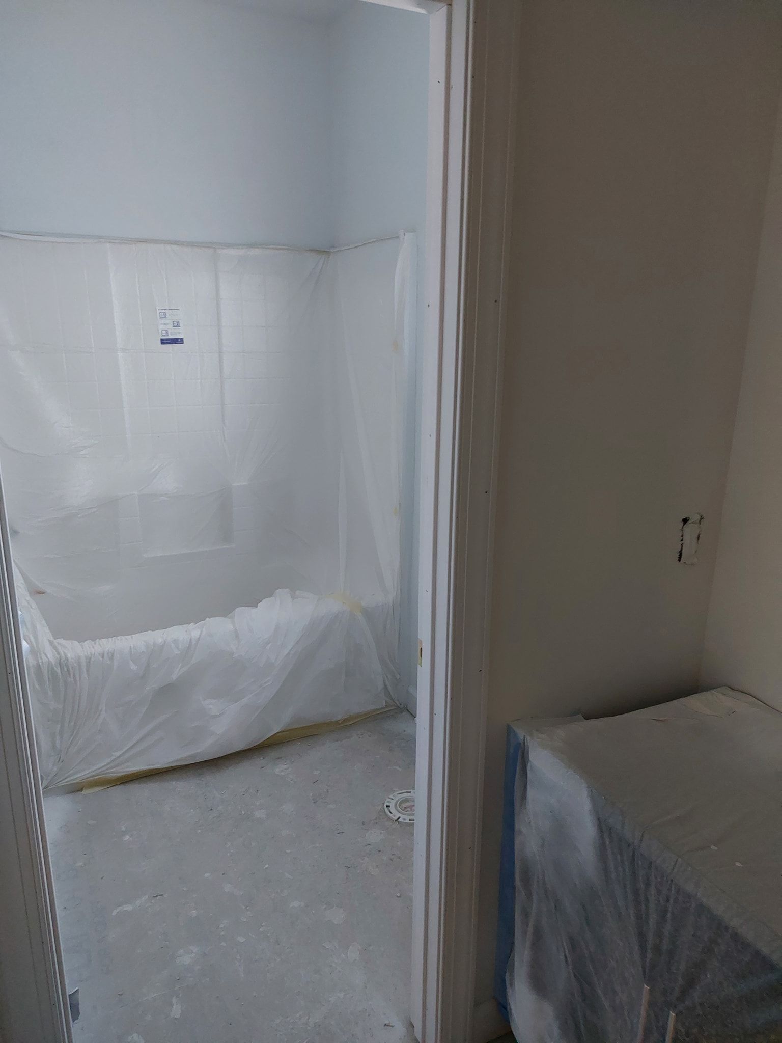 Small hallway and room under renovation, with plastic-covered walls and floor and a covered object in the corner