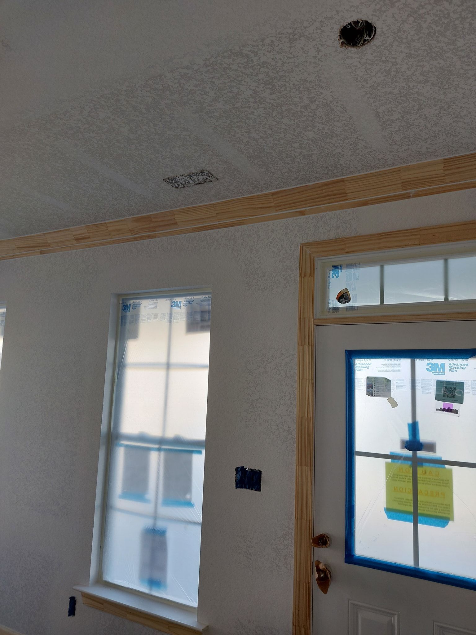 Empty room with a window and door, white textured walls, and blue painter’s tape around the door glass.