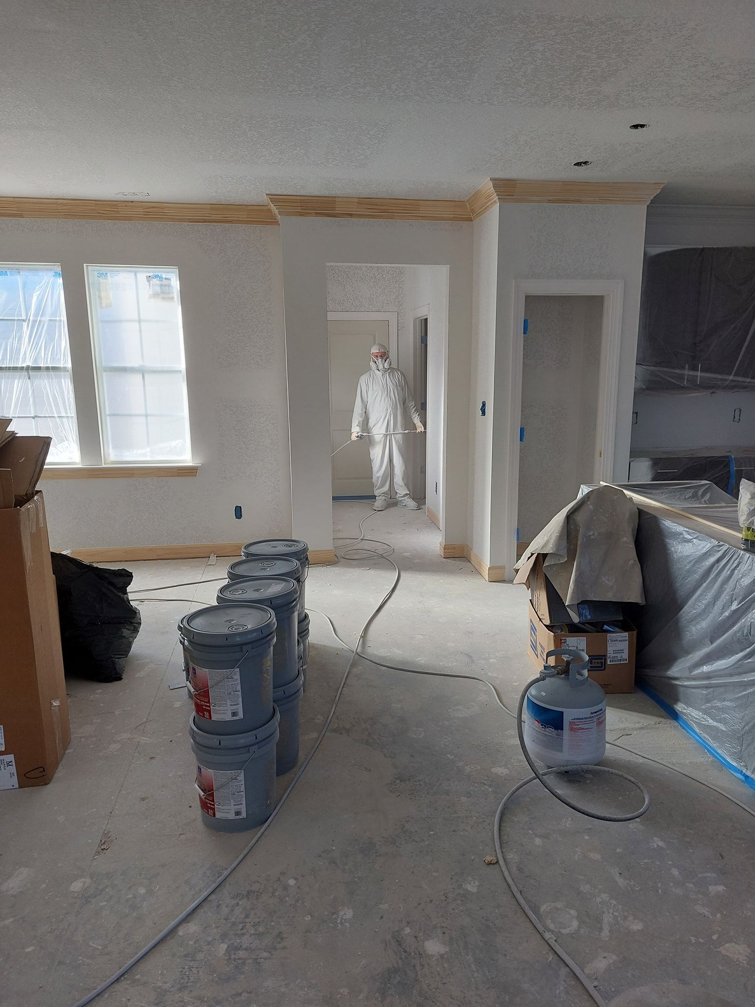 Partially renovated room with unfinished drywall, windows, a doorway, and construction materials on the floor