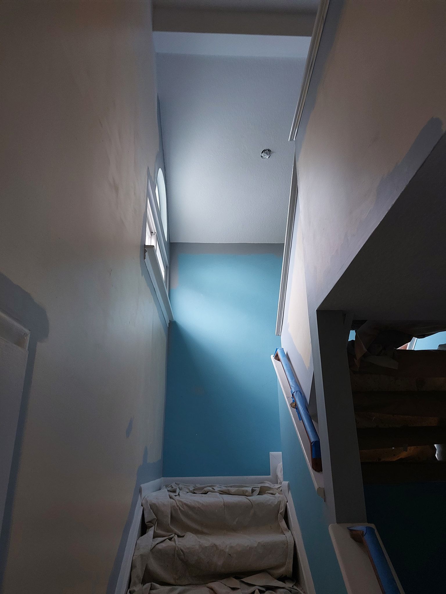 Stairwell with blue walls, white railing, and a beige chair at the bottom.