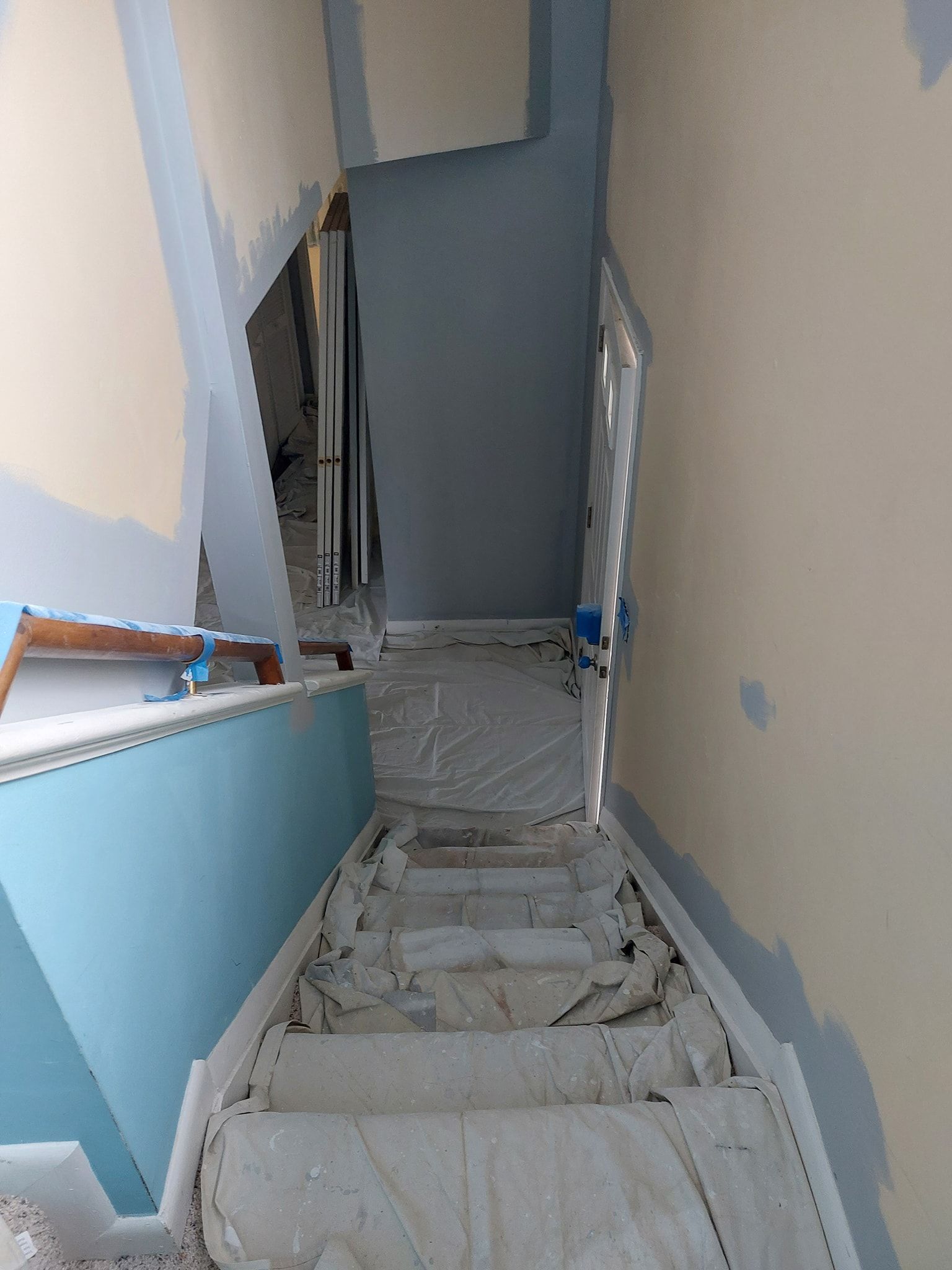 Narrow interior stairwell under construction with blue walls and unfinished steps covered in dust and debris
