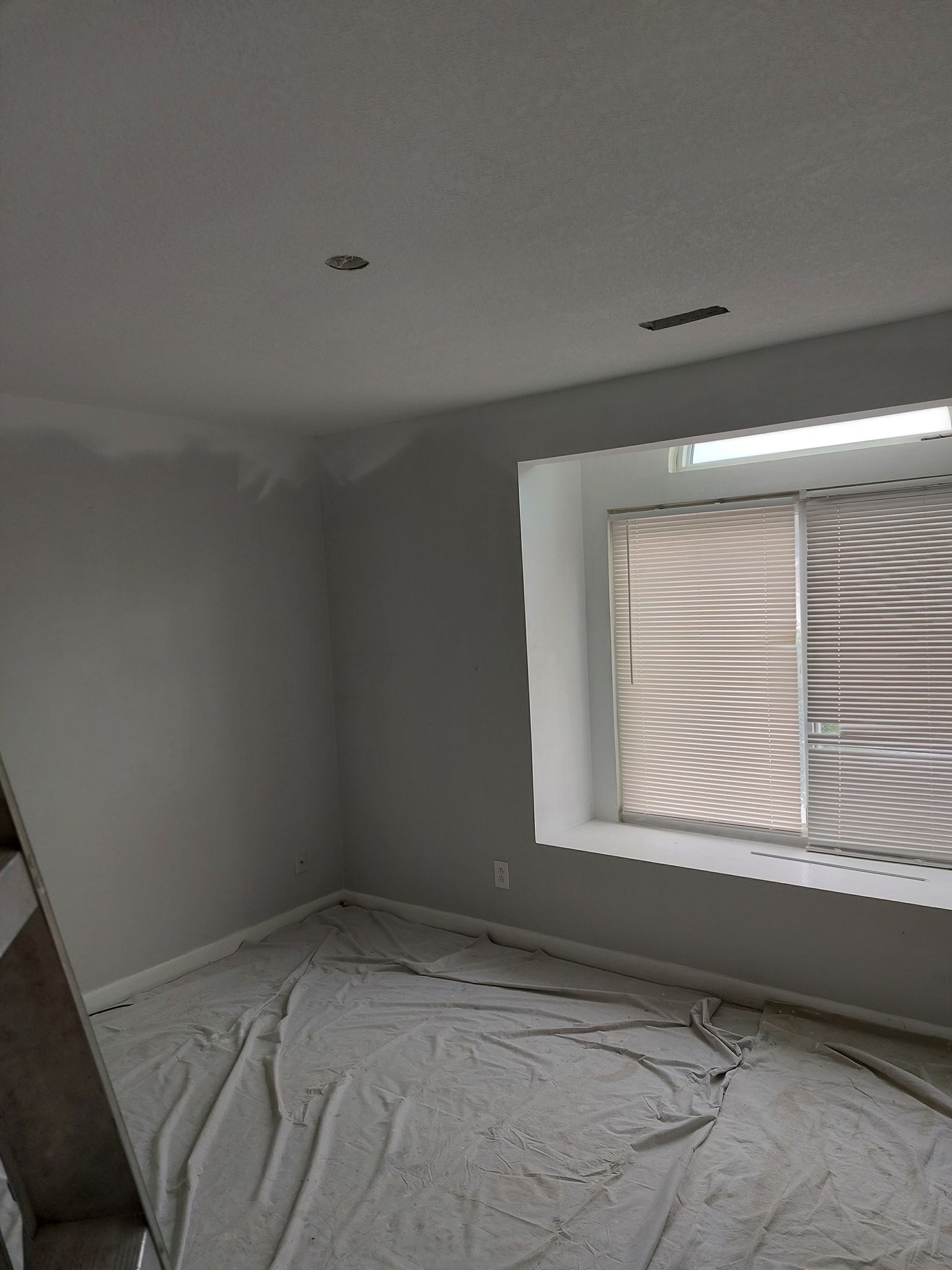 Empty gray room under renovation with plastic-covered floor and a window covered by sheeting