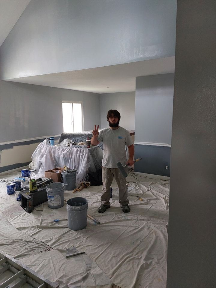 Painter standing in a room under renovation with covered floors, paint buckets, and fresh gray walls