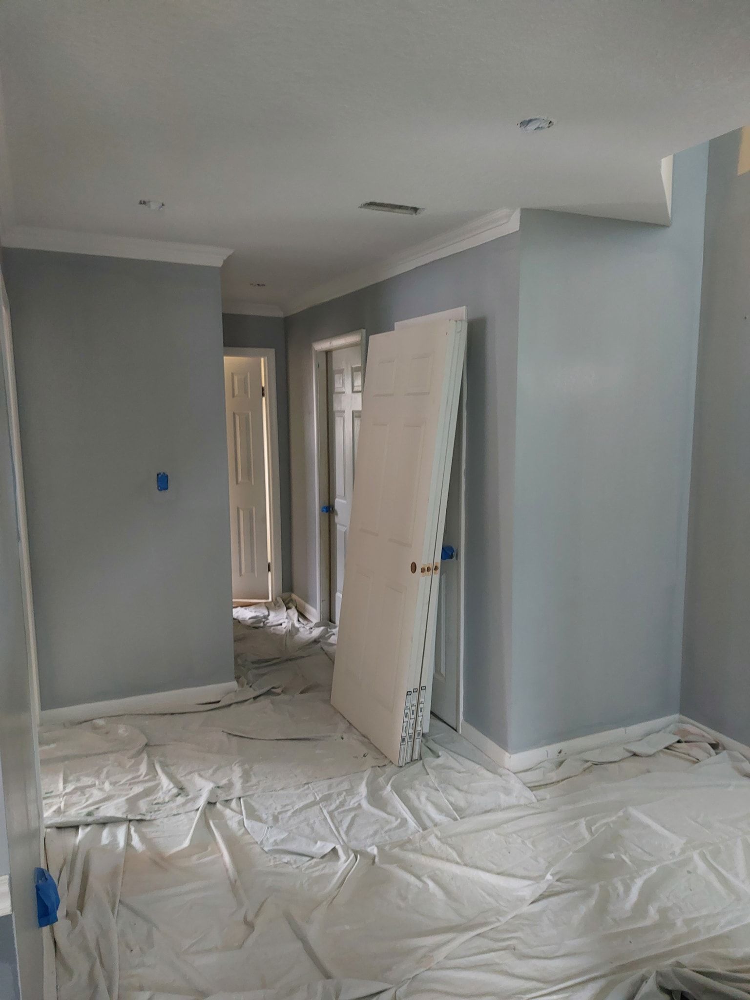 Renovation in progress in a gray room, with plastic-covered floor and a door leaning against the wall.