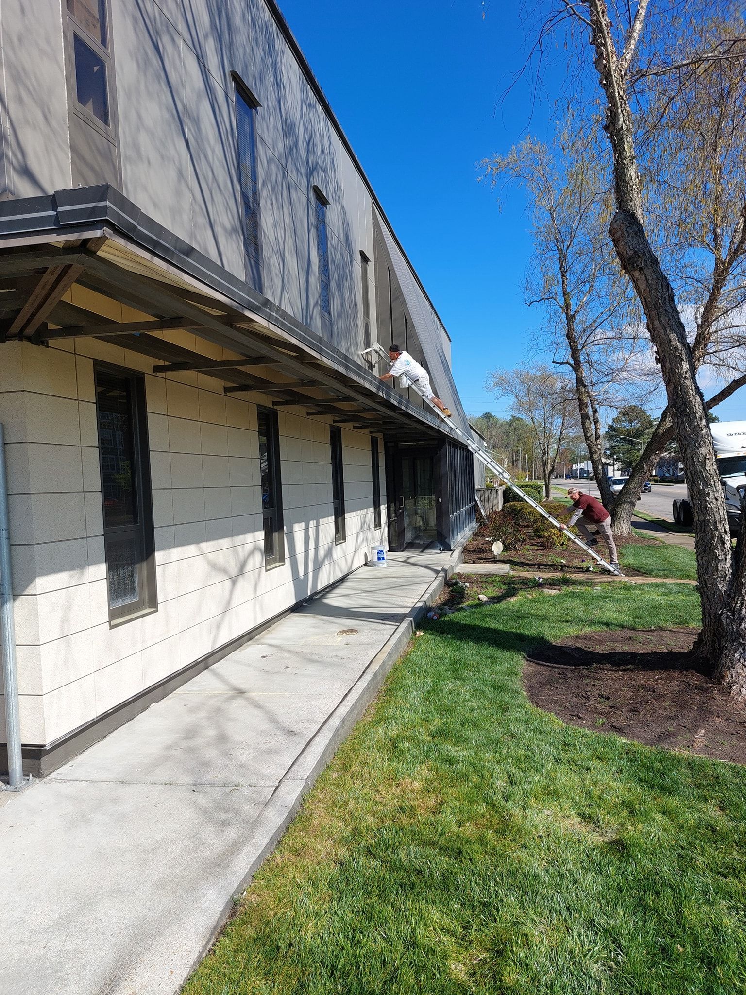 Apartment building exterior with white siding, concrete walkway, grass, and bare trees under a blue sky
