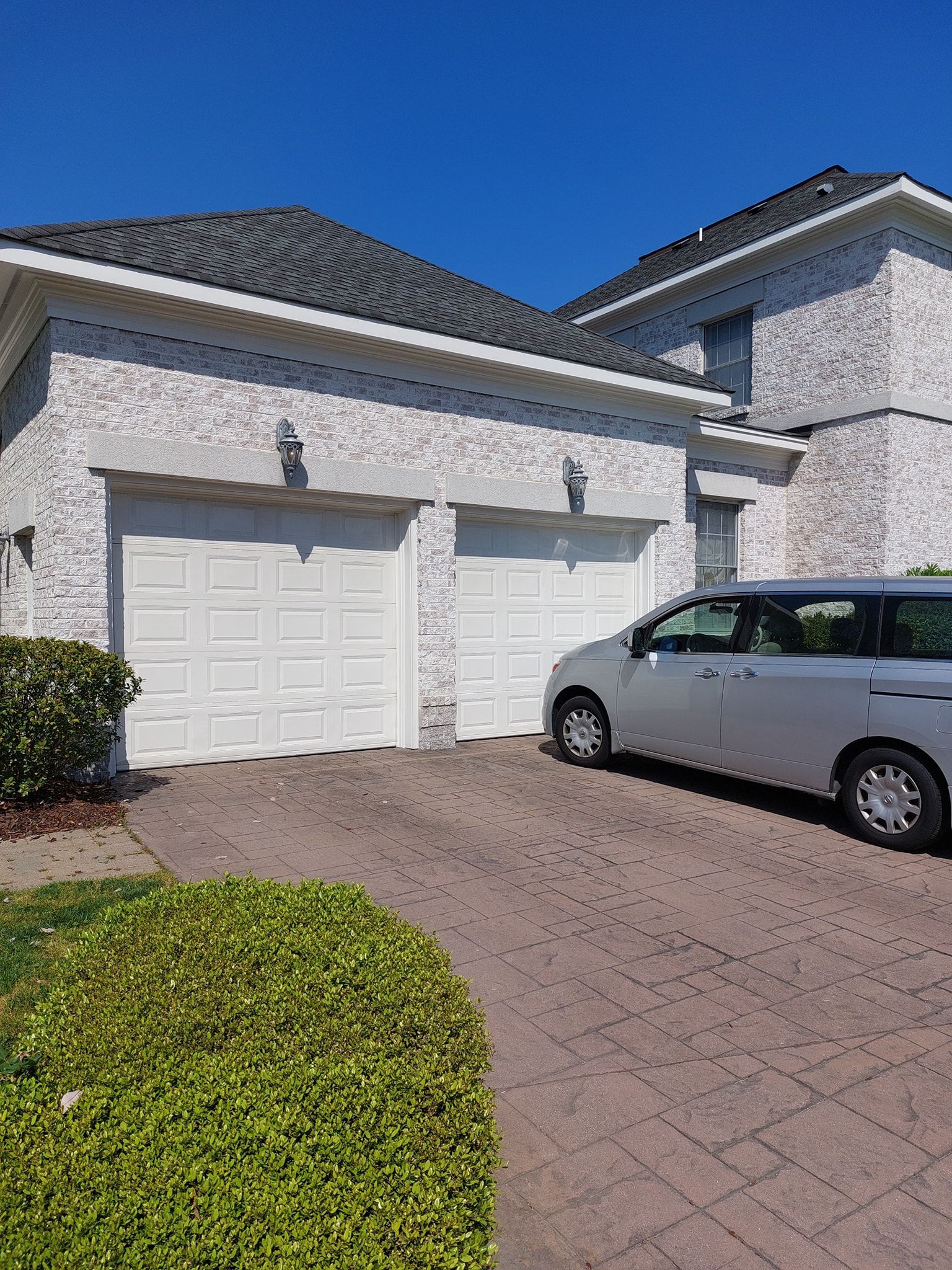 Suburban townhouse garage with a silver minivan parked in the driveway under a blue sky