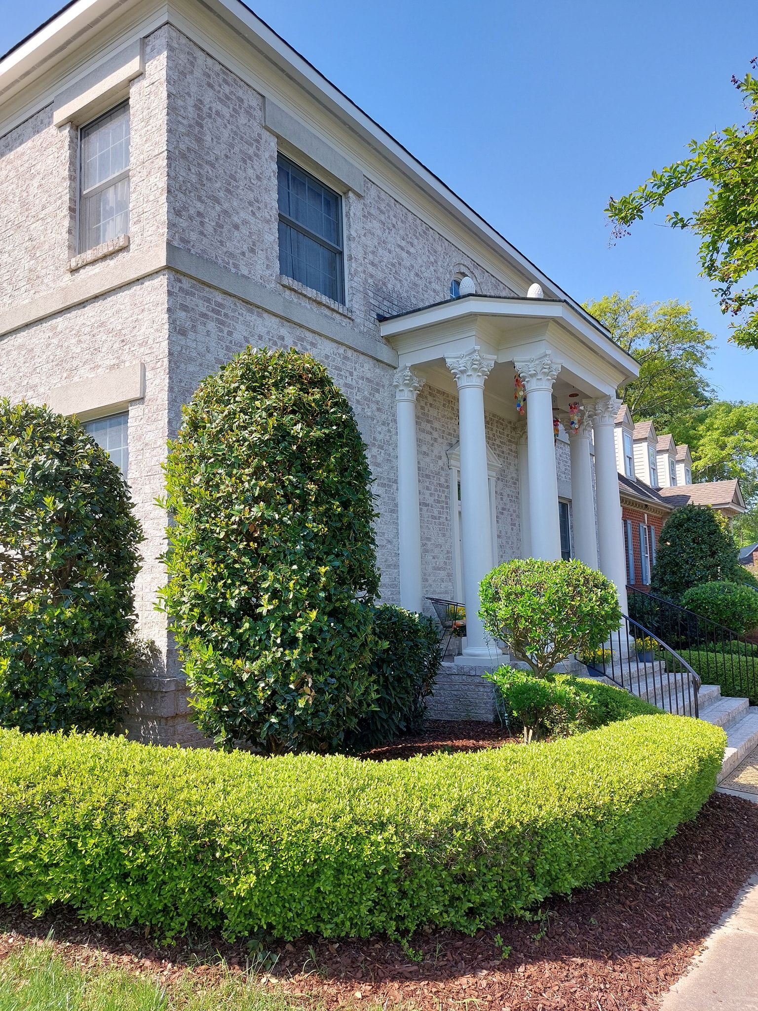 Stone house with white columns and manicured shrubs in a sunny front yard