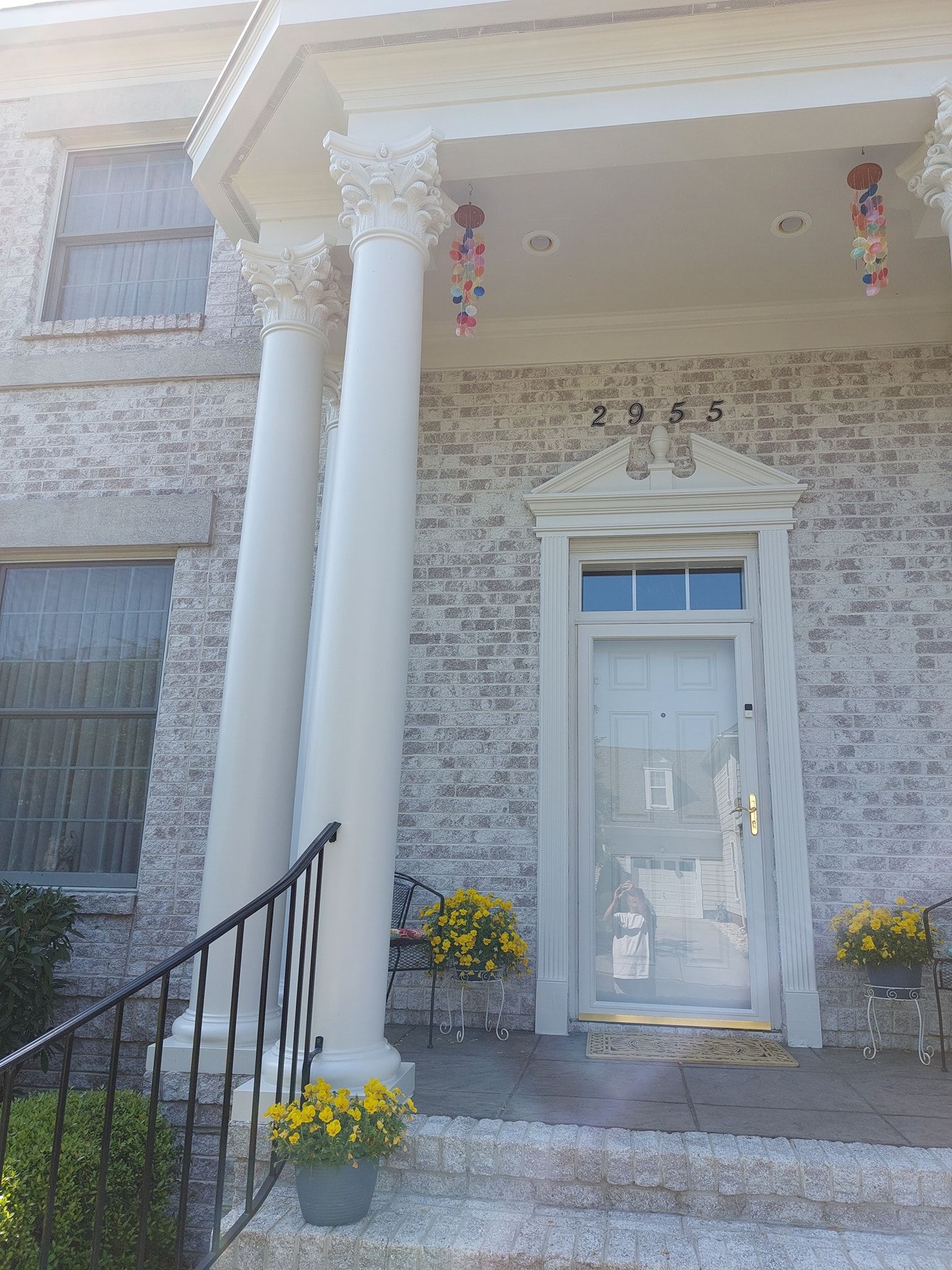 Stone house front porch with white columns, glass door, and yellow potted flowers on the steps