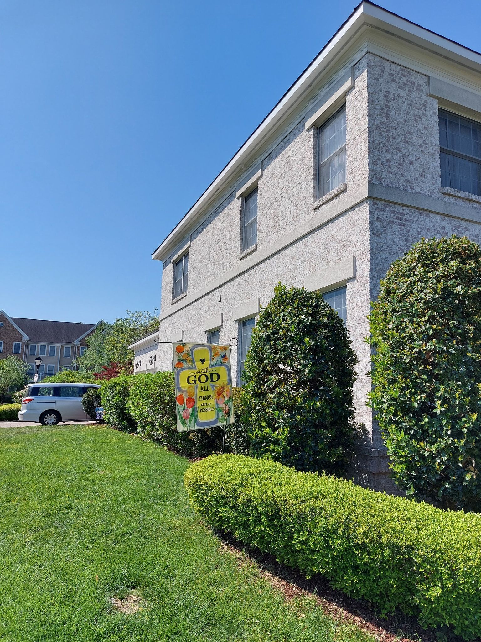 Suburban house with manicured shrubs, green lawn, and a parked car under a clear blue sky