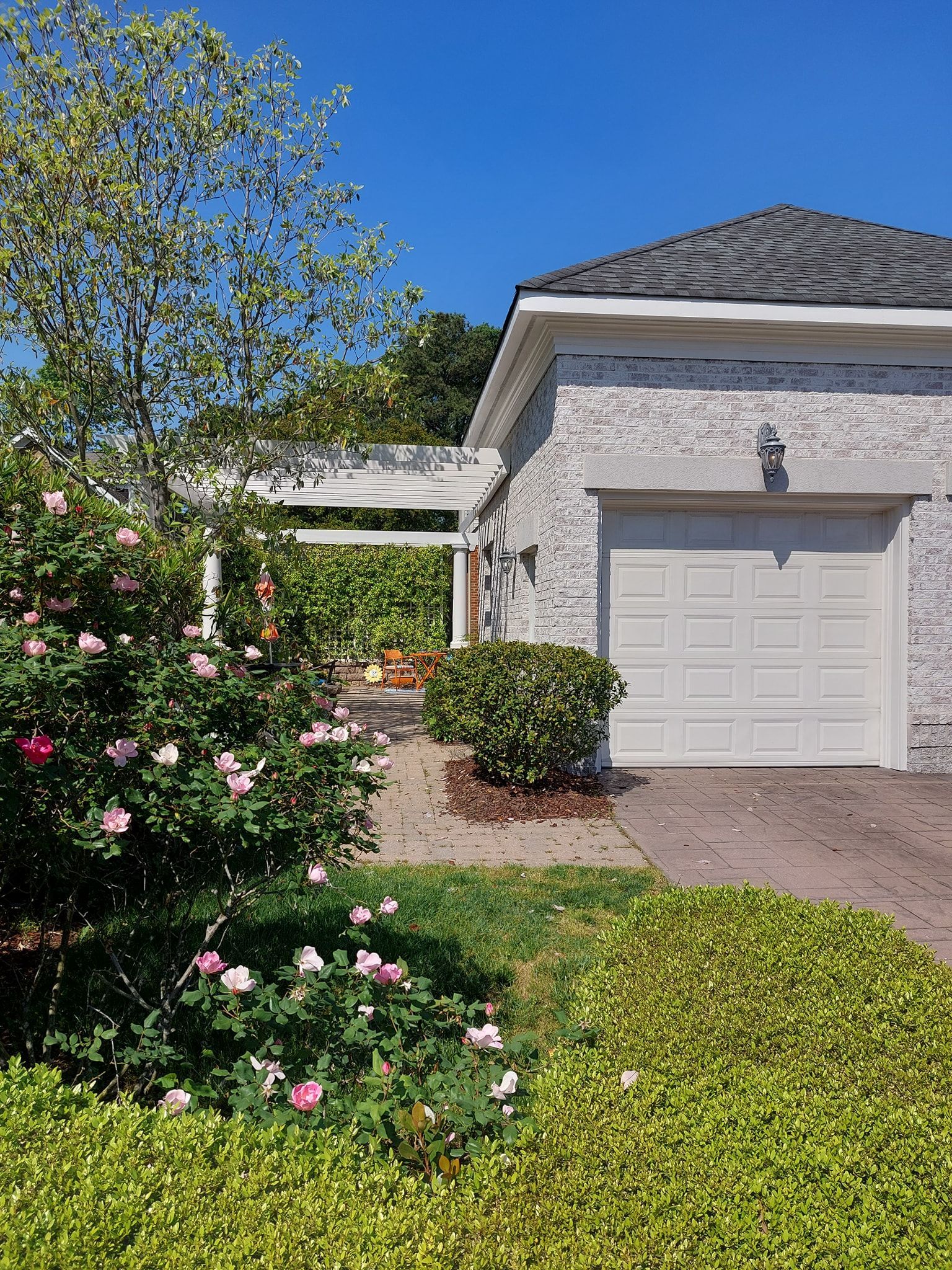 Suburban house with white garage, gray roof, and pink flowering bushes in the front yard