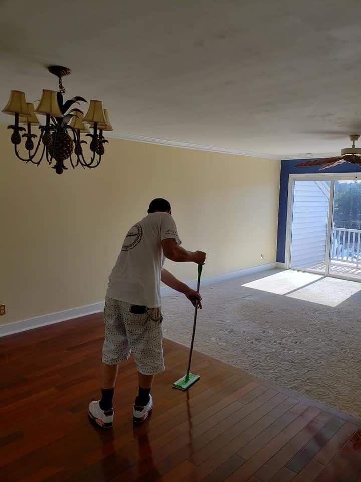 Person mopping hardwood floors in an empty living room with chandelier and sliding glass doors.