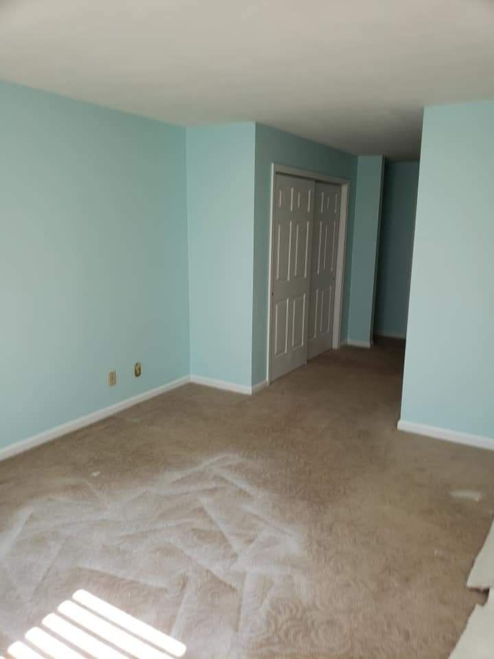 Empty bedroom with light blue walls, beige carpet, and a gray closet door.