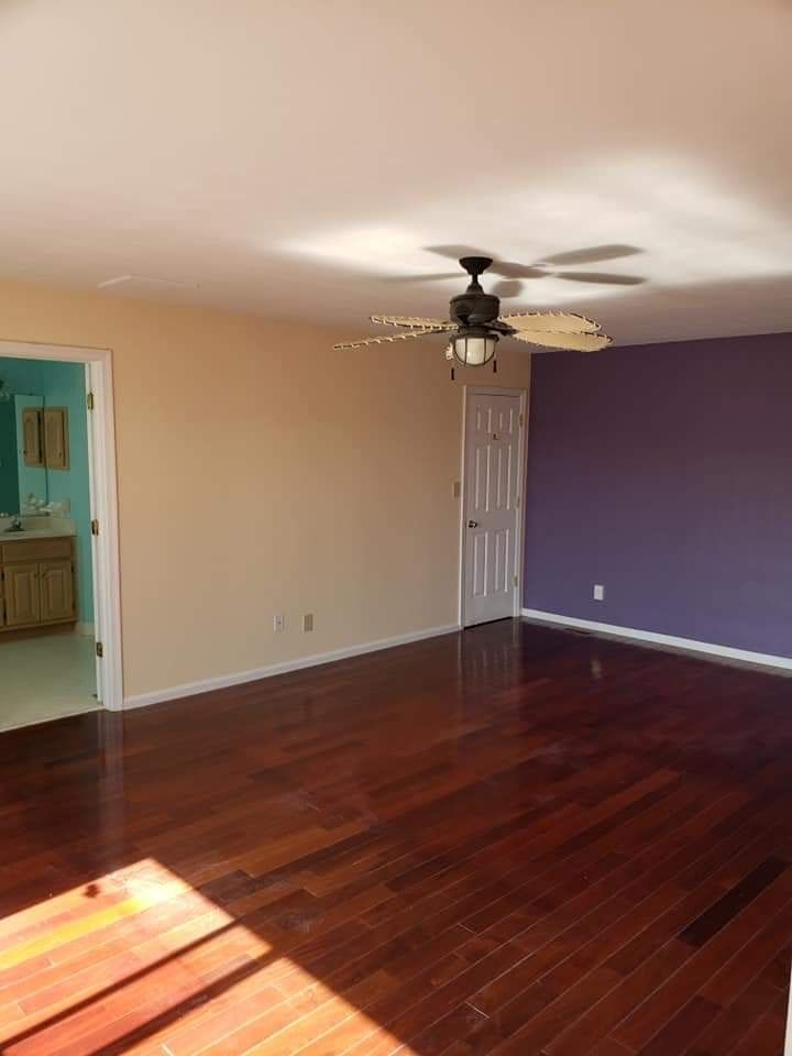 Empty room with dark hardwood floors, beige and purple walls, and a ceiling fan near a white door