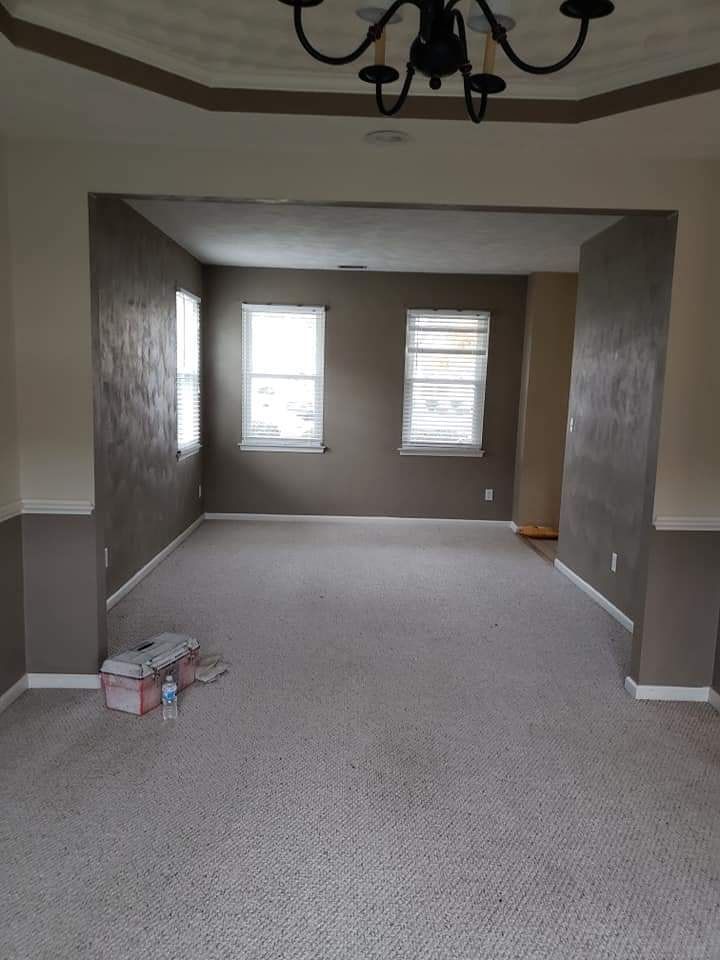 Empty carpeted living room with two windows and an open doorway, viewed from an adjoining room