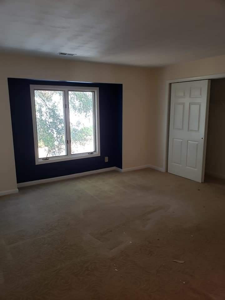 Empty beige bedroom with carpet, window, and white closet doors
