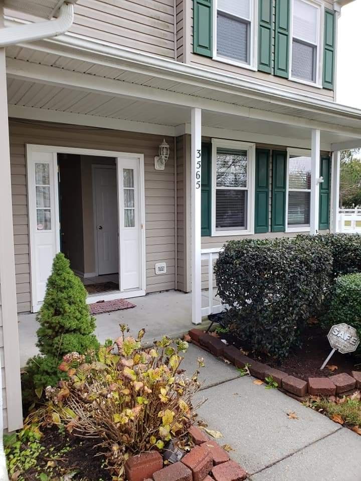 Front porch of a townhouse with white trim, green shutters, and a small garden path.