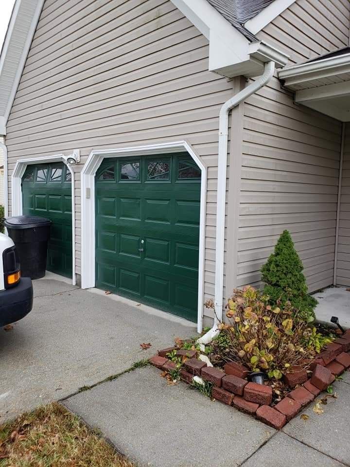 Two green garage doors on a beige house beside a driveway and small brick flower bed