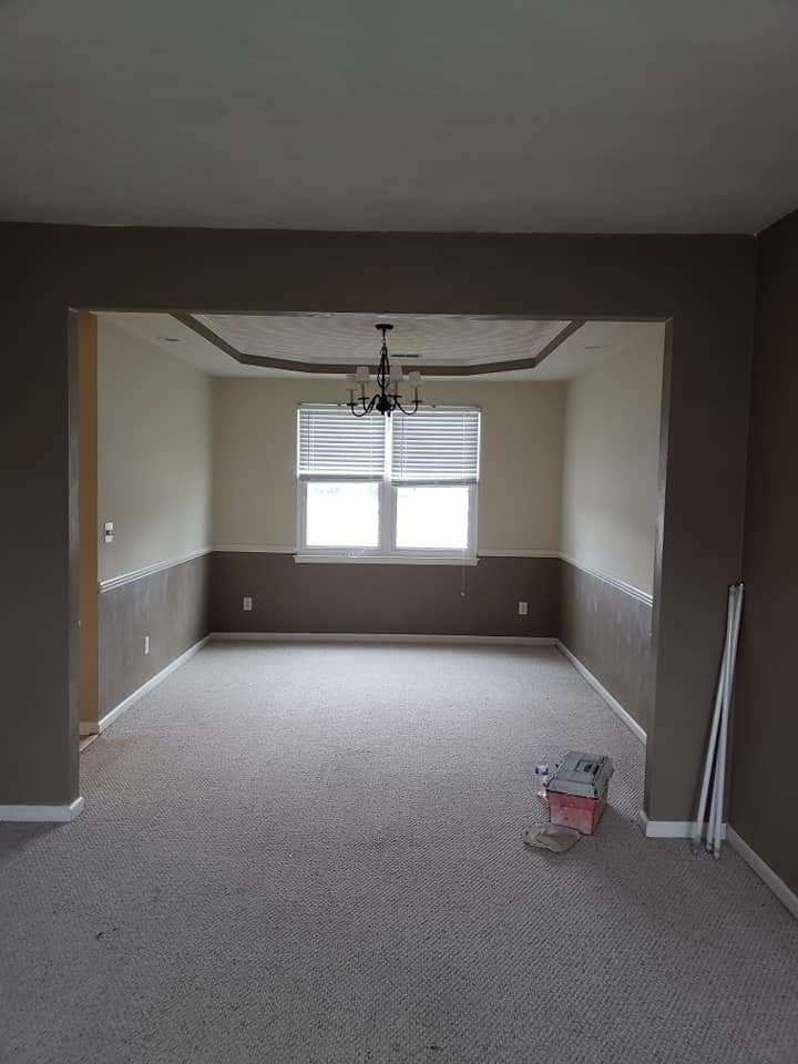 Empty carpeted dining room with gray walls, a chandelier, and a window at the far end.