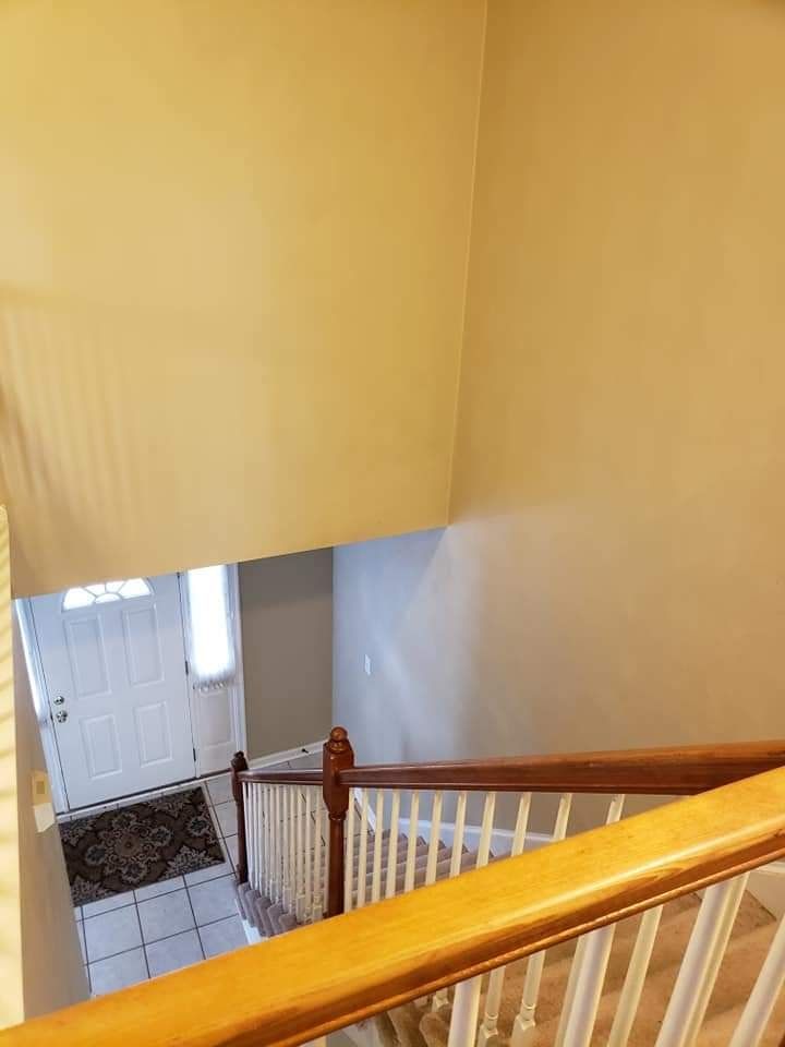 Stairwell with beige walls, wooden railing, and a white front door at the bottom.