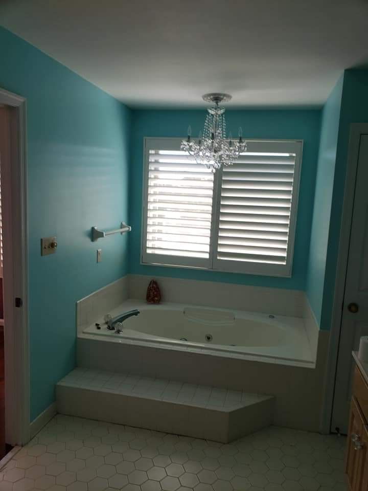 Empty teal bathroom with a white jacuzzi tub, chandelier, and window blinds.