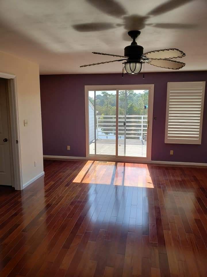 Empty room with hardwood floors, purple accent wall, ceiling fan, and sunlit sliding glass door.