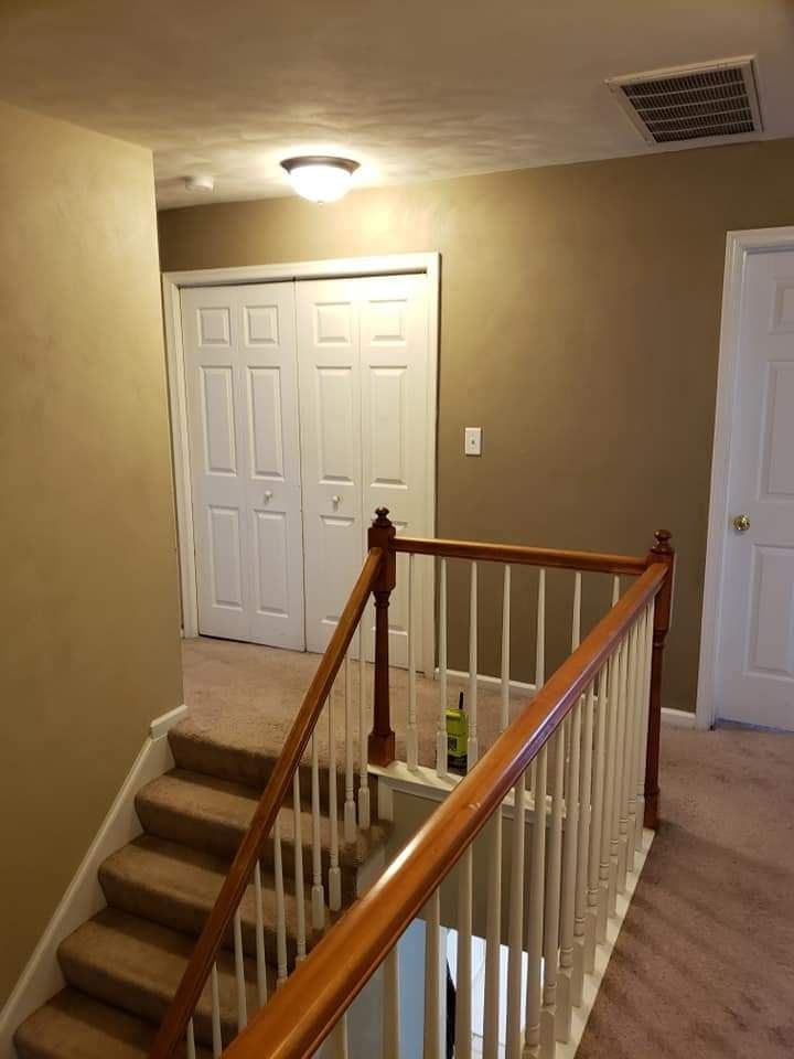 Stair landing in a beige hallway with white closet doors and a wooden railing.