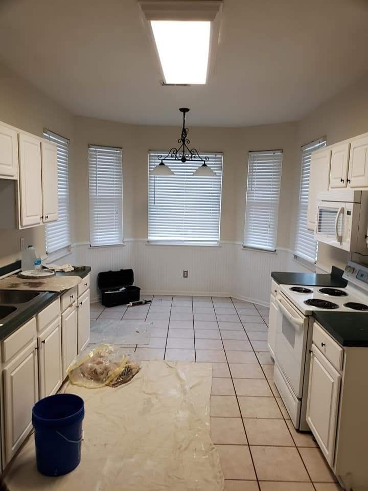Empty kitchen with white cabinets, tiled floor, fluorescent ceiling light, and a blue bucket on the left.