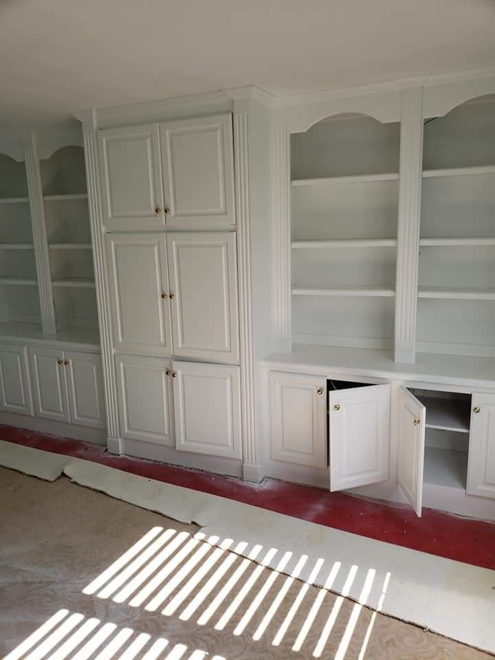 Built-in white cabinets and shelves in a room with sunlight streaming through blinds onto the floor