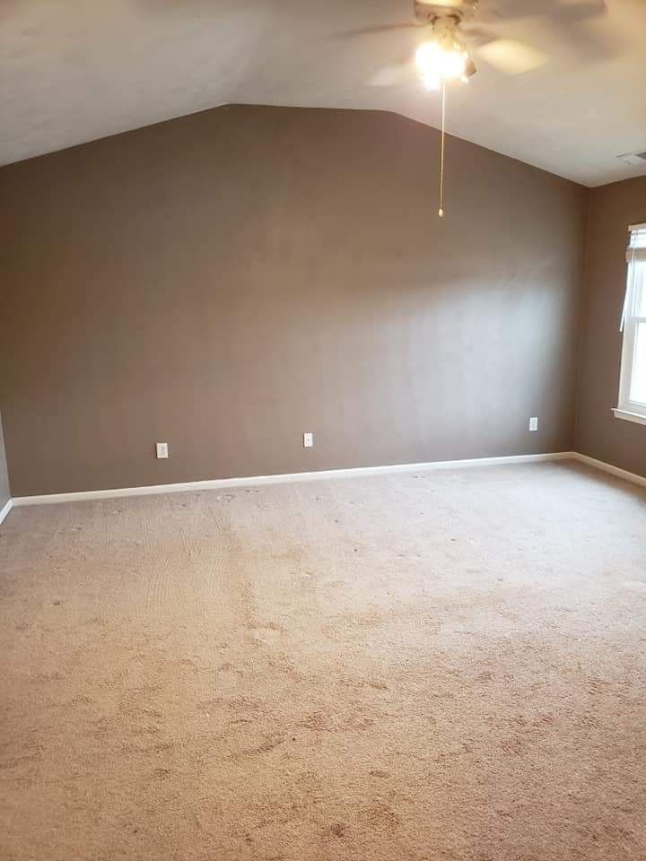 Empty beige bedroom with carpeted floor, sloped ceiling, ceiling fan, and a window on the right.
