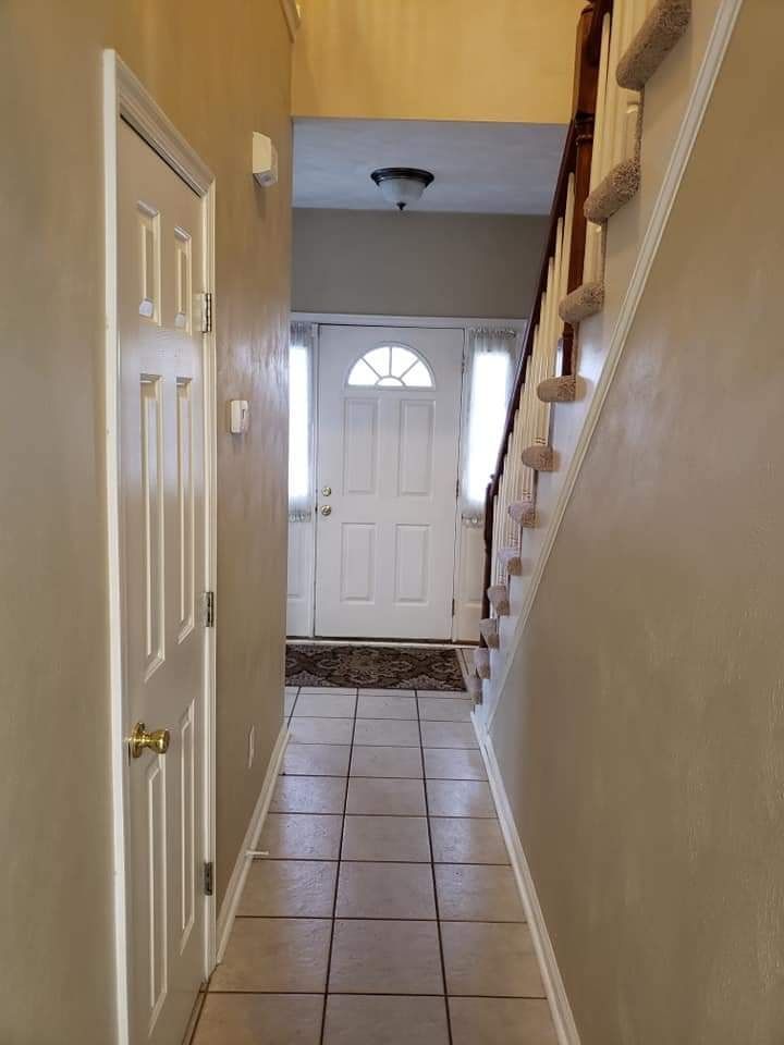Narrow hallway with tiled floor, beige walls, front door, and staircase on the right.