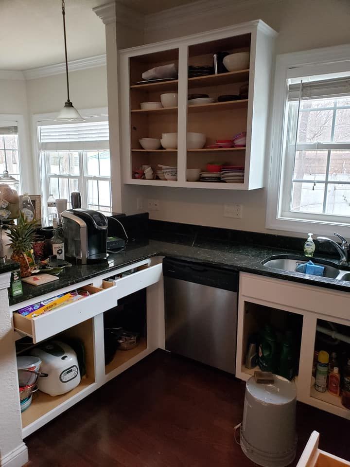 Compact kitchen corner with black countertops, open shelves, a sink, and a small white stove/oven.