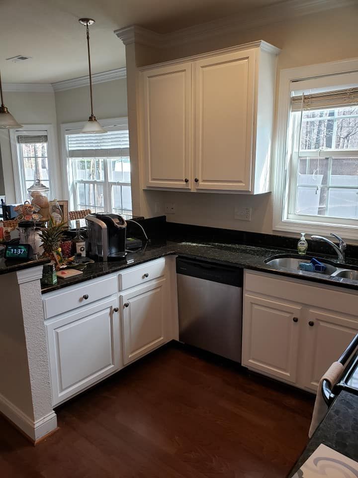 Bright kitchen corner with white cabinets, black countertops, sink, dishwasher, and hardwood floor.