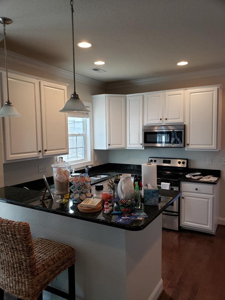 Bright kitchen with white cabinets, black countertops, stainless appliances, and a cluttered island table.