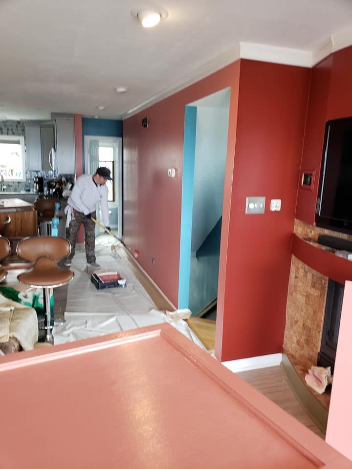 Person painting a red-walled hallway with a roller, plastic-covered floor in a home interior