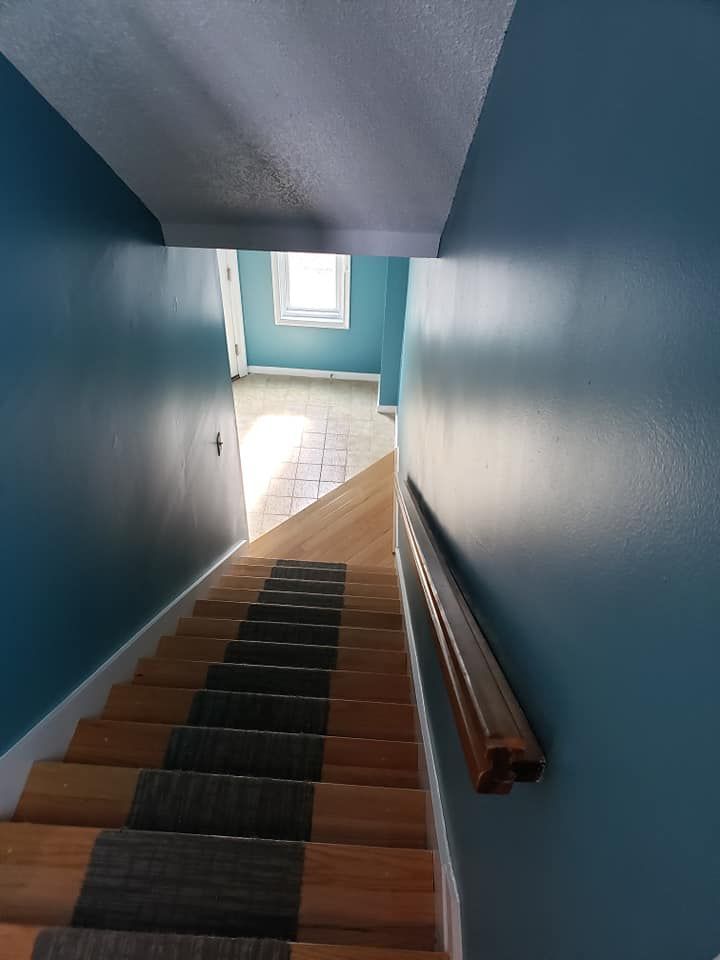 Staircase with blue walls, wooden steps, and a handrail leading to a bright window at the top