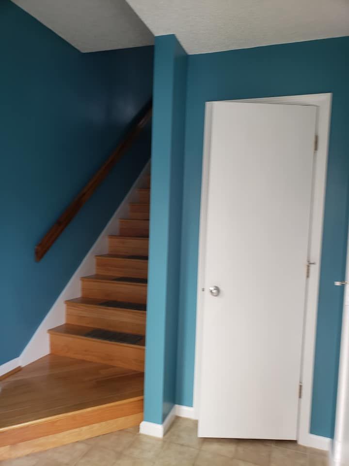 Staircase with wooden steps and dark railing beside a white door in a blue hallway.