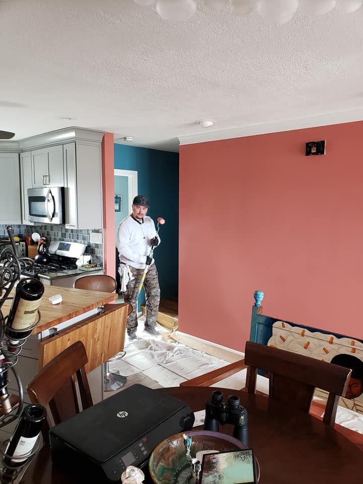 Person standing in a kitchen and dining area with coral walls and white ceiling, holding a tool or phone.