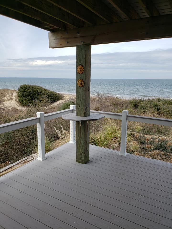 Covered seaside deck with white railings, wooden post, and ocean view beyond dunes