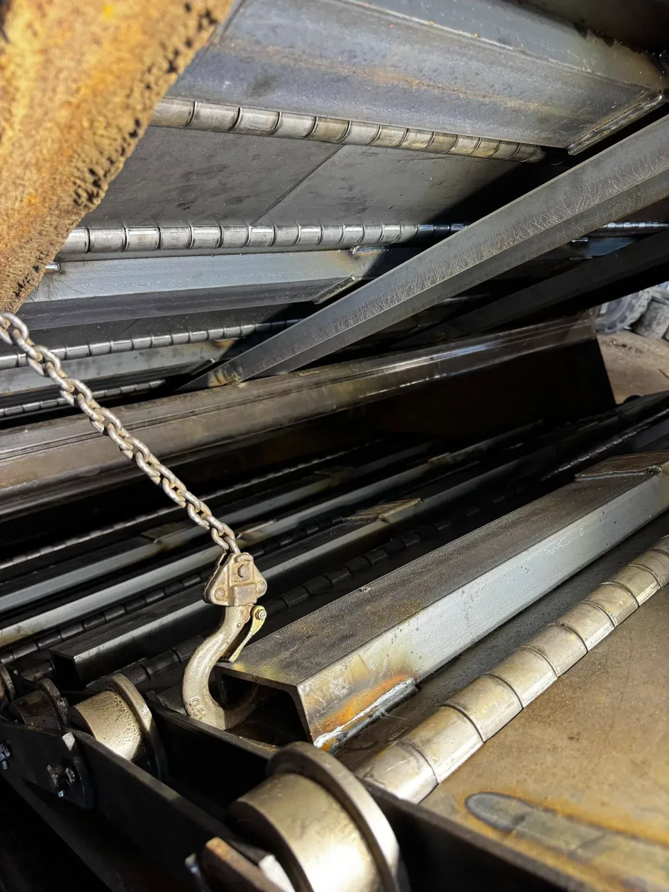 Metal parts of a machine, with a chain and hook. Dark, industrial setting.
