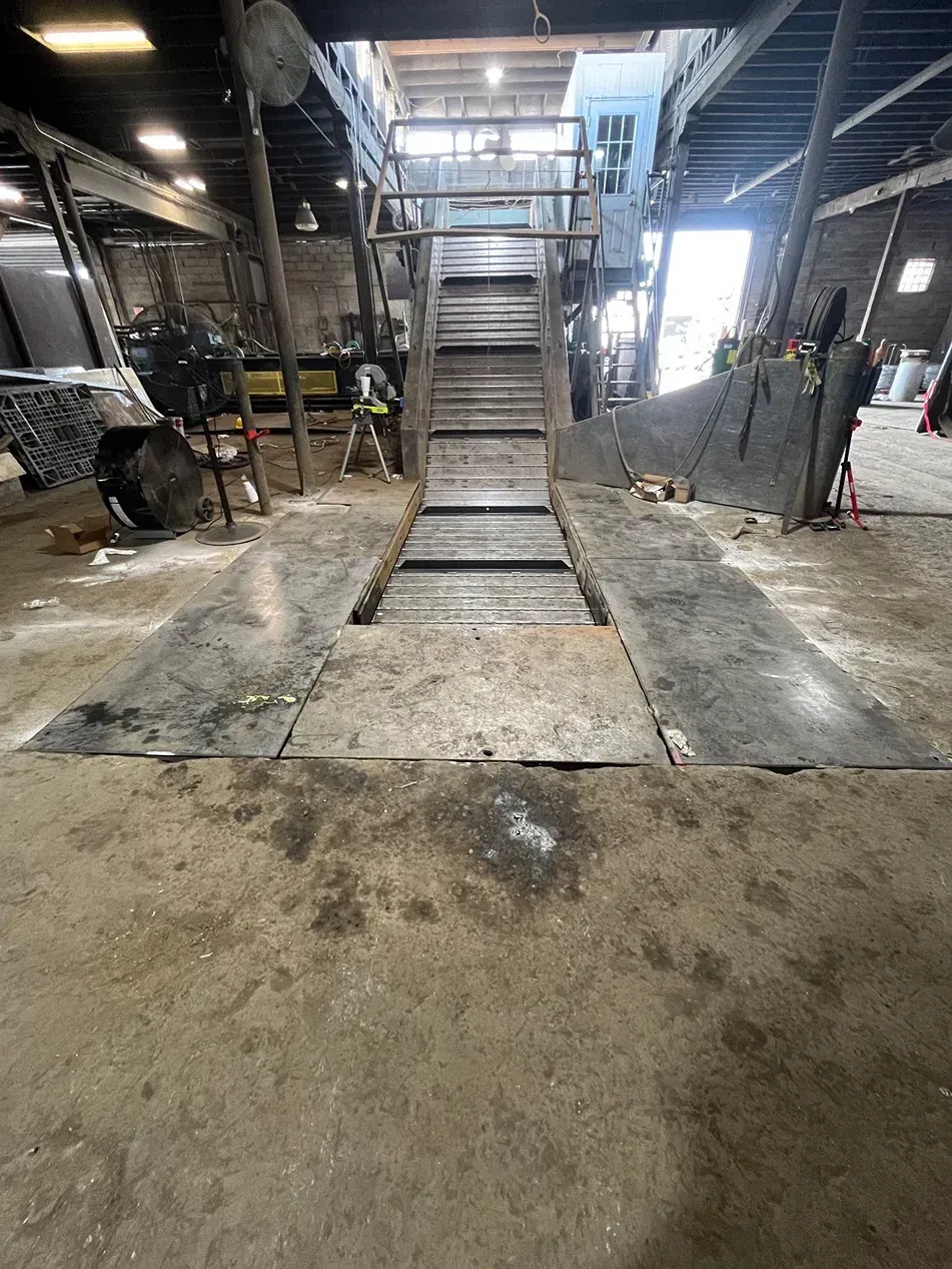 Interior shot of an industrial building with a raised platform. Dark concrete floor and machinery are visible.