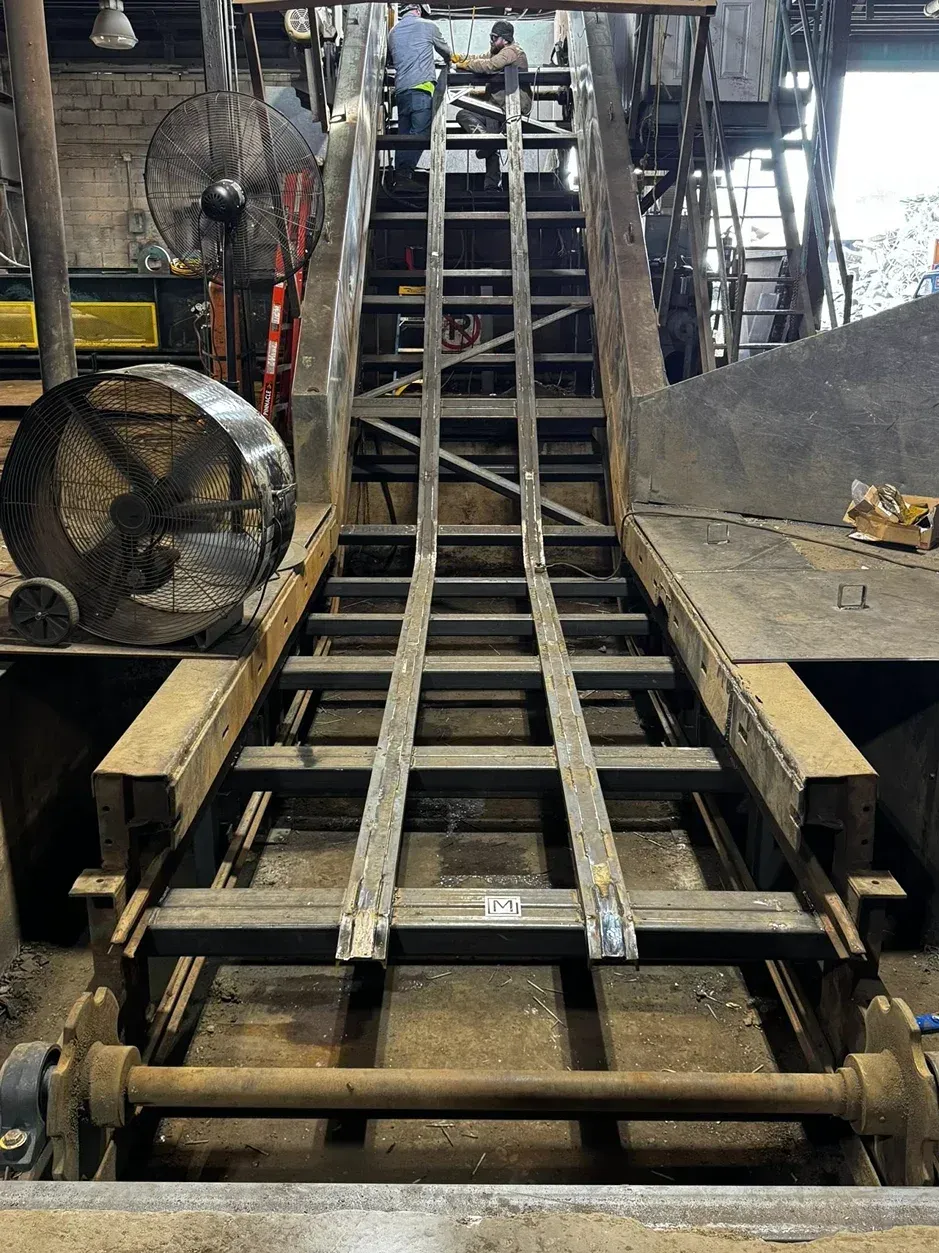 Metal ladder structure under construction in a factory, with workers in background.