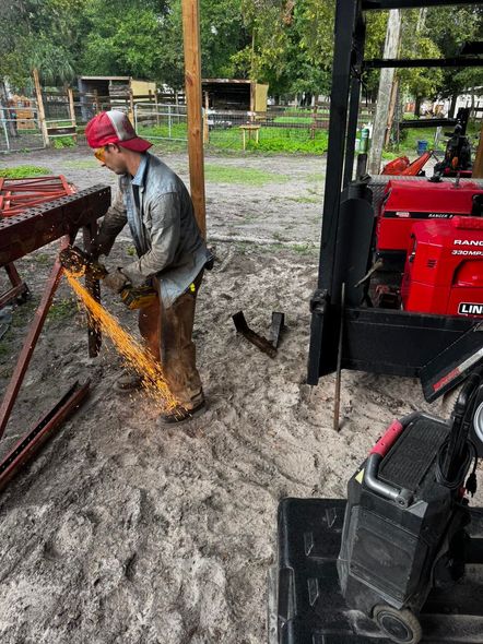 Man cutting metal with sparks flying outdoors, wearing safety gear.