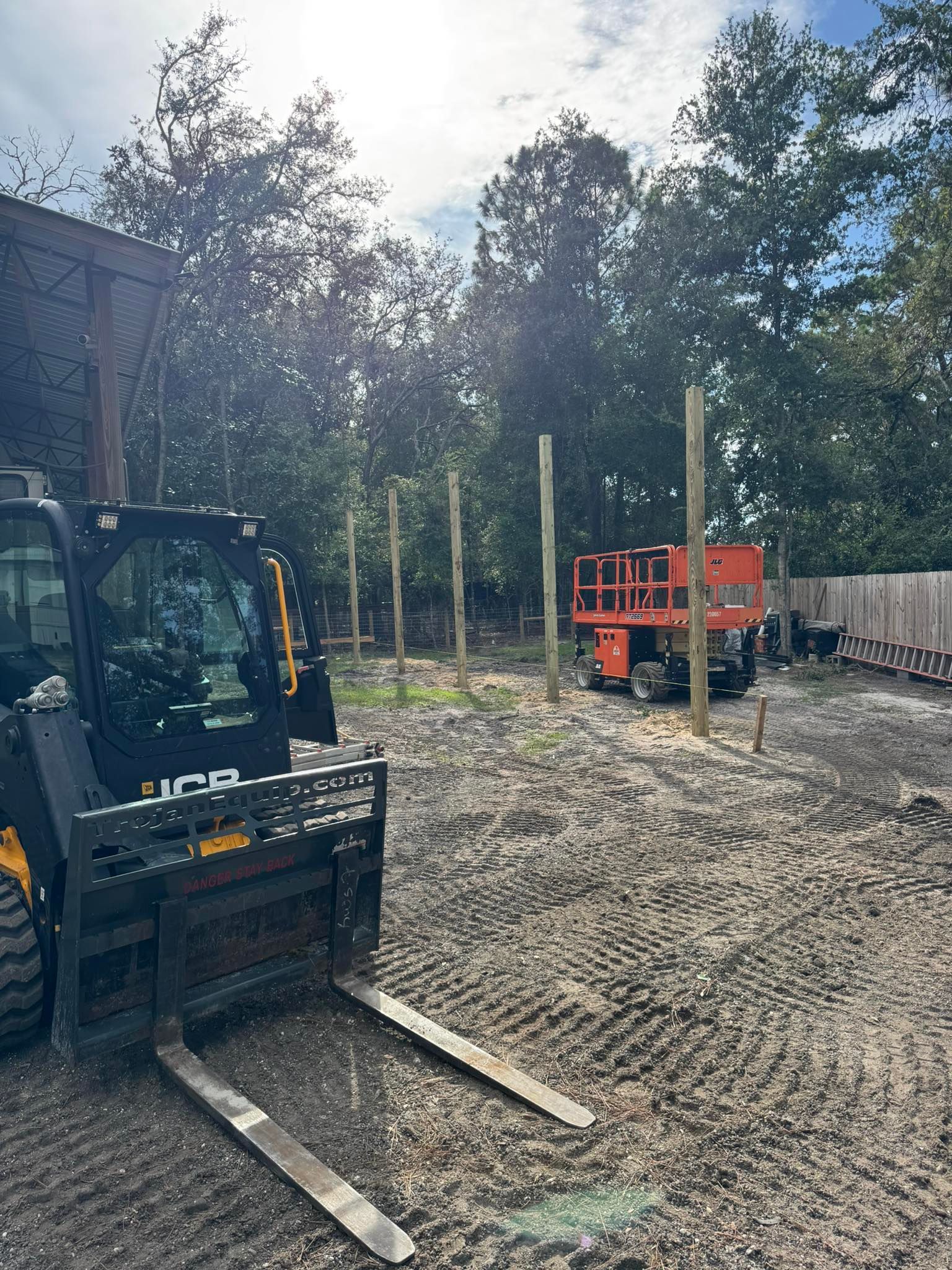 Construction site with a skid steer, lift, and wooden posts.