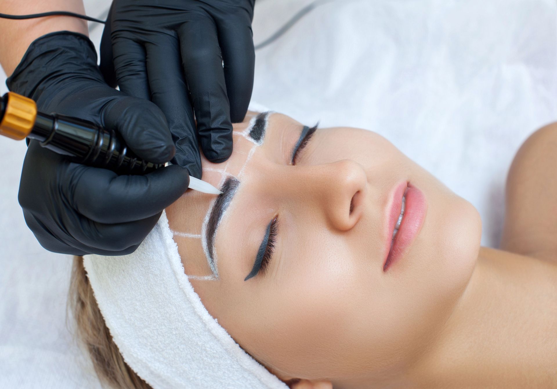 Una persona que se somete a un procedimiento profesional de tatuaje permanente de cejas con contornos marcados en su piel.